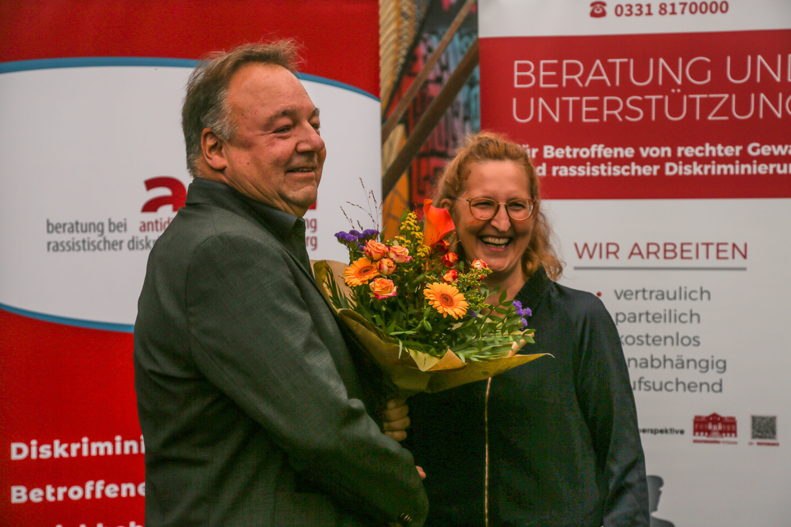 Alfred Roos, Leiter der Koordinierungsstelle „Tolerantes Brandenburg“, überreicht Judith Porath, Geschäftsführerin der Opferperspektive, einen Blumenstrauß