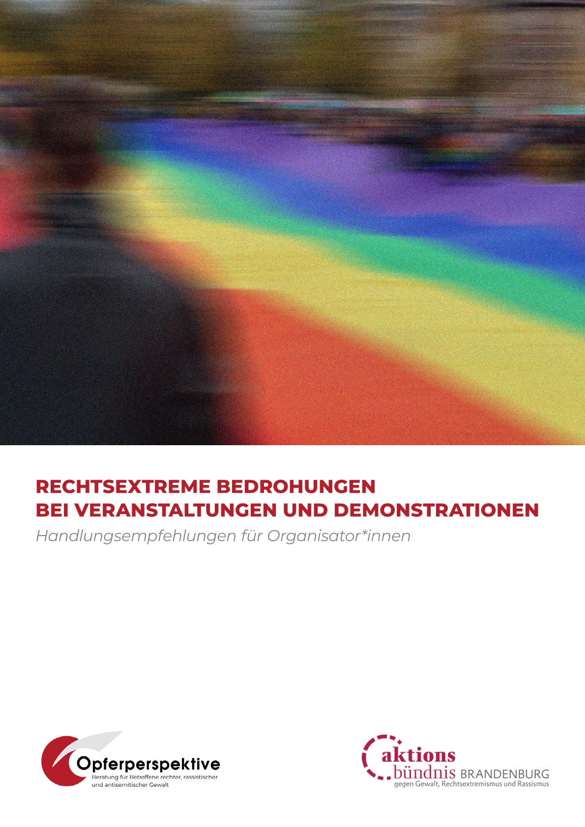Verschwommen im Hintergrund eine große Regenbogenfahne, an den Seiten Menschen auf einer Versammlung.